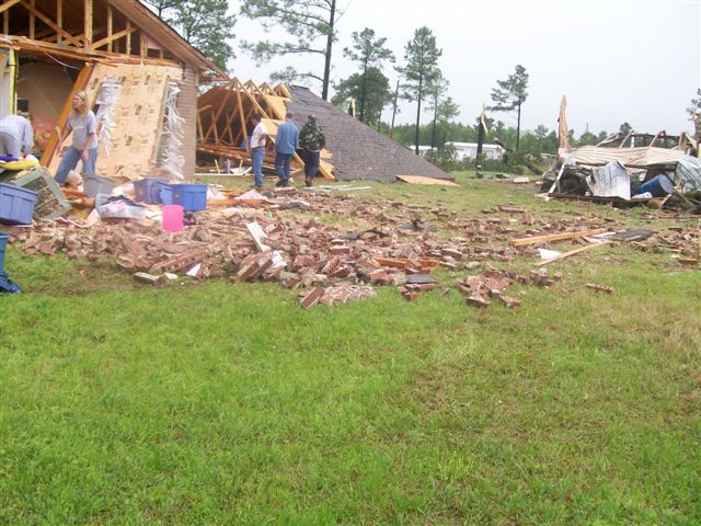 House walls torn off, roofs blown down, people assessing the damage.